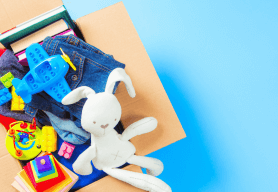 a cardboard box of various children's toys and clothes including a toy plane and a white bunny. Background is sky blue.